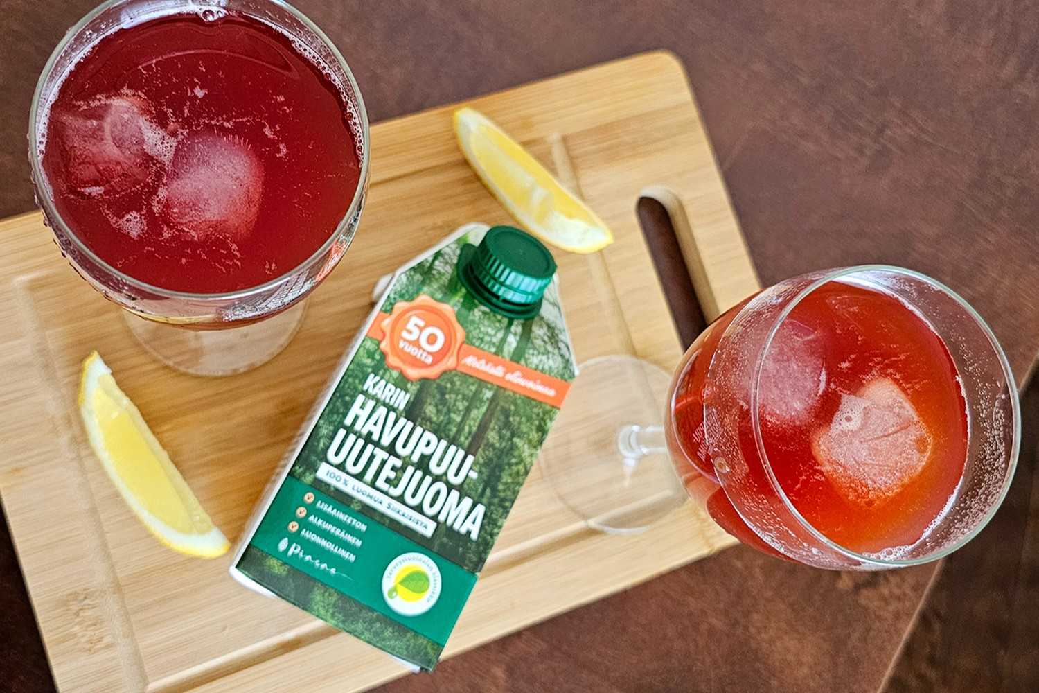 Karin Havupuu-uutejuomasta tehdyt alkoholittomat drinkit, mukana sitruunaa ja omenamehua. drinkit ja tölkki leikkuulaudan päällä sekä sitruunanpuolikkaat.